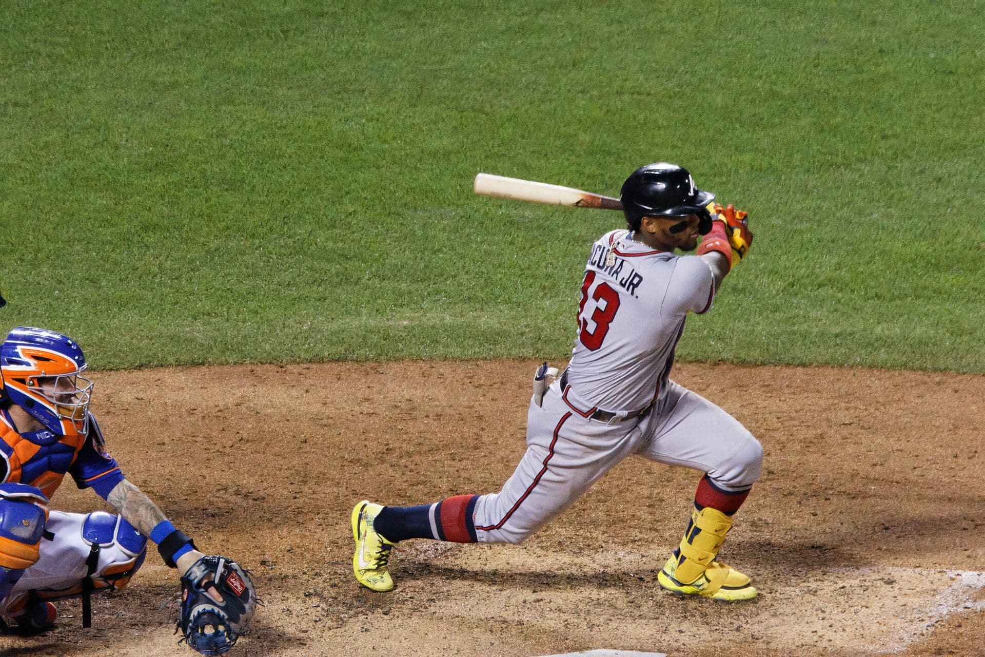 Atlanta Braves outfielder Ronald Acuna Jr., number 13 in a gray Atlanta road uniform, following through on a swing with the catcher crouched behind him