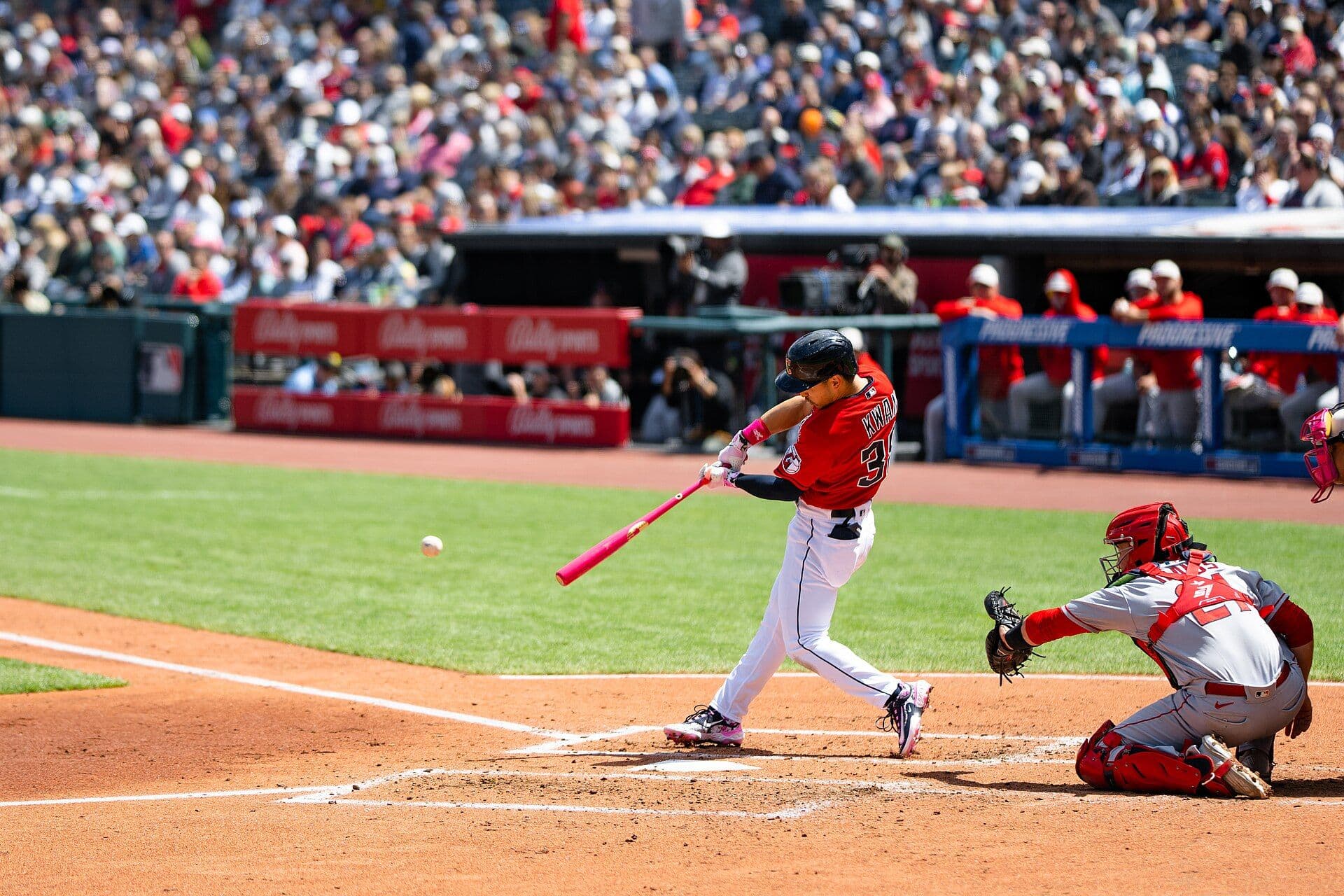 Cleveland Guardians outfielder Steven Kwan mid-swing making contact with a pitch, wearing a red Cleveland jersey with his name and number on the back