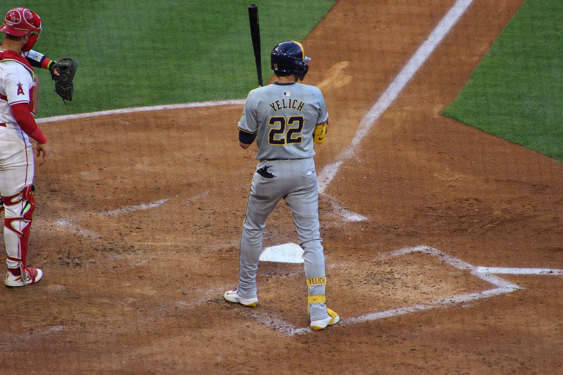 Christian Yelich stands in the batter's box in a gray Milwaukee Brewers road uniform, number 22 on his back, with the catcher waiting beside home plate.