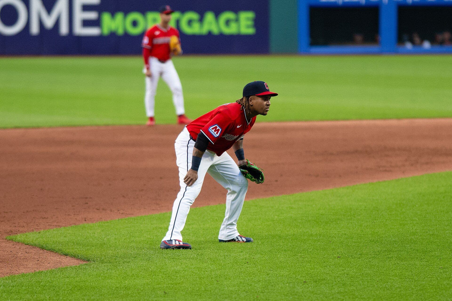 Cleveland Guardians third baseman José Ramírez in a red home jersey and navy cap, crouched in a ready stance at third base during a 2026 game.