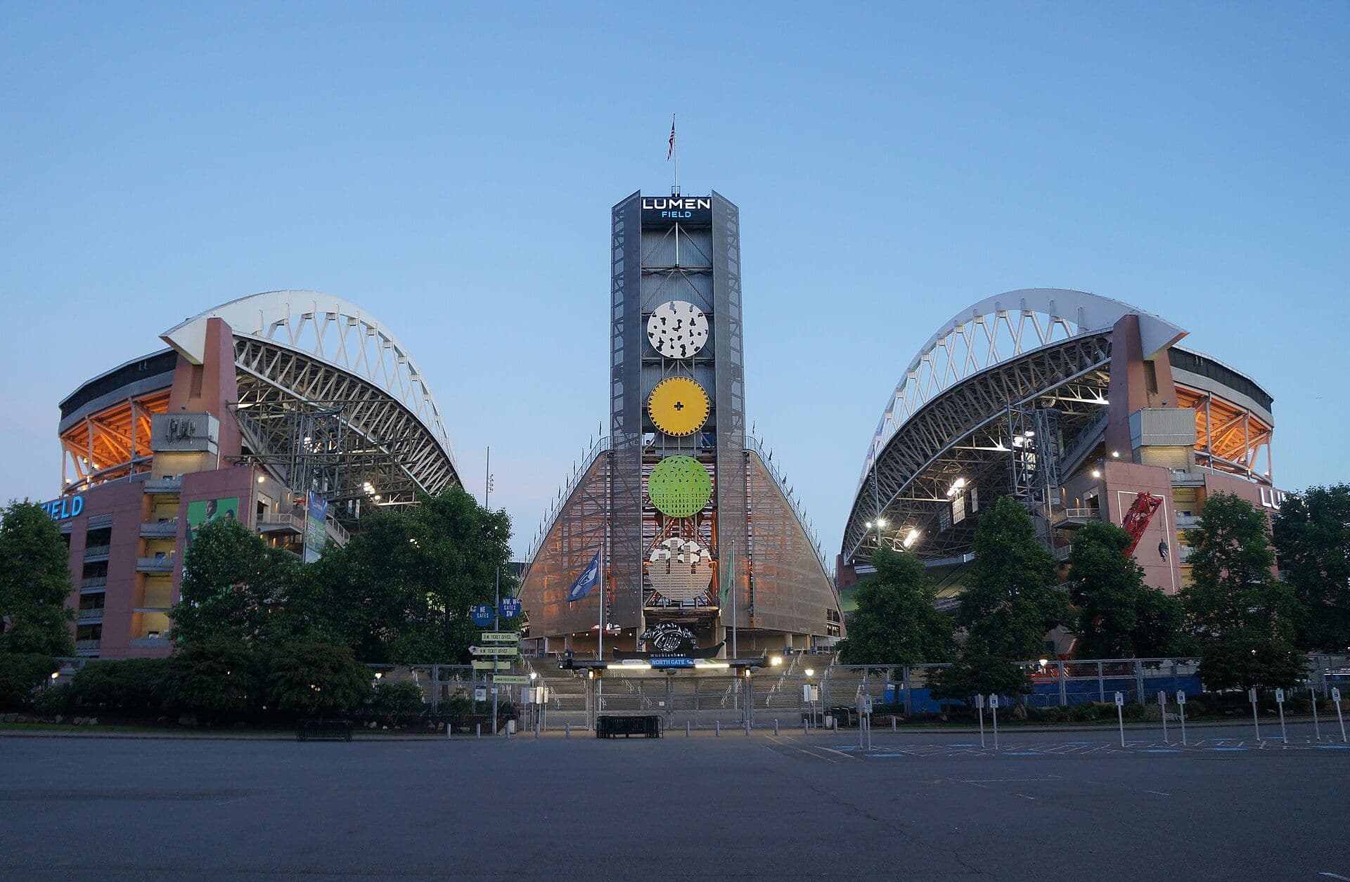 The north entrance of Lumen Field in Seattle at dusk, with the illuminated Lumen Field sign on the tower between the stadium's two roof arches.