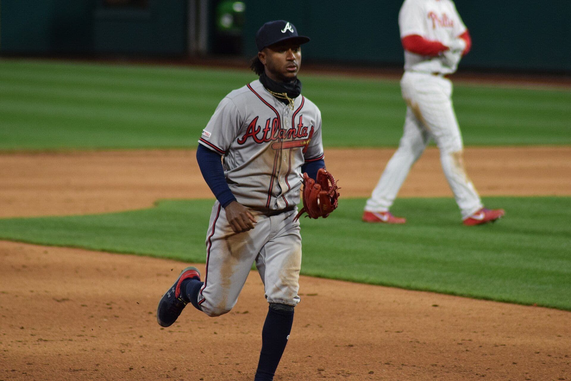 Atlanta Braves infielder Ozzie Albies jogging across the infield with his glove, in a gray Atlanta road uniform