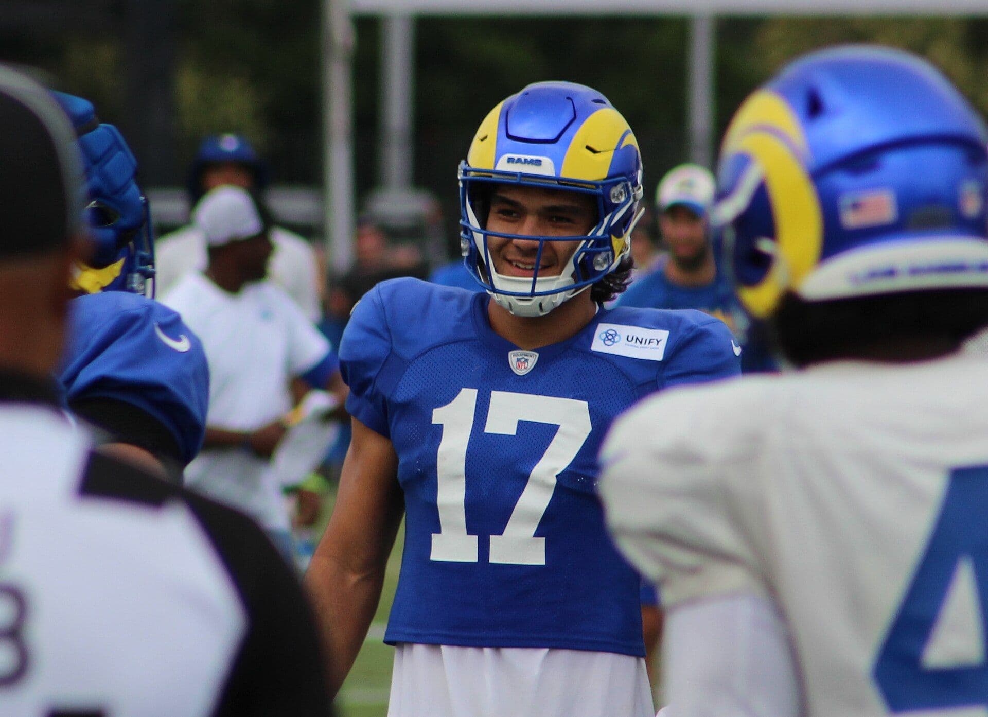 Los Angeles Rams wide receiver Puka Nacua in a blue number 17 practice jersey and Rams helmet, smiling on the practice field.