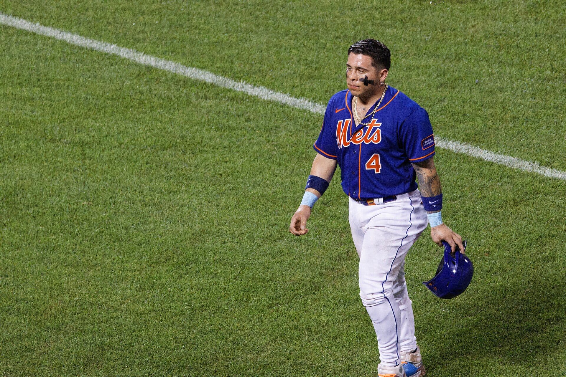 New York Mets catcher Francisco Alvarez, wearing the blue Mets jersey with number 4, walks across the grass holding his batting helmet.