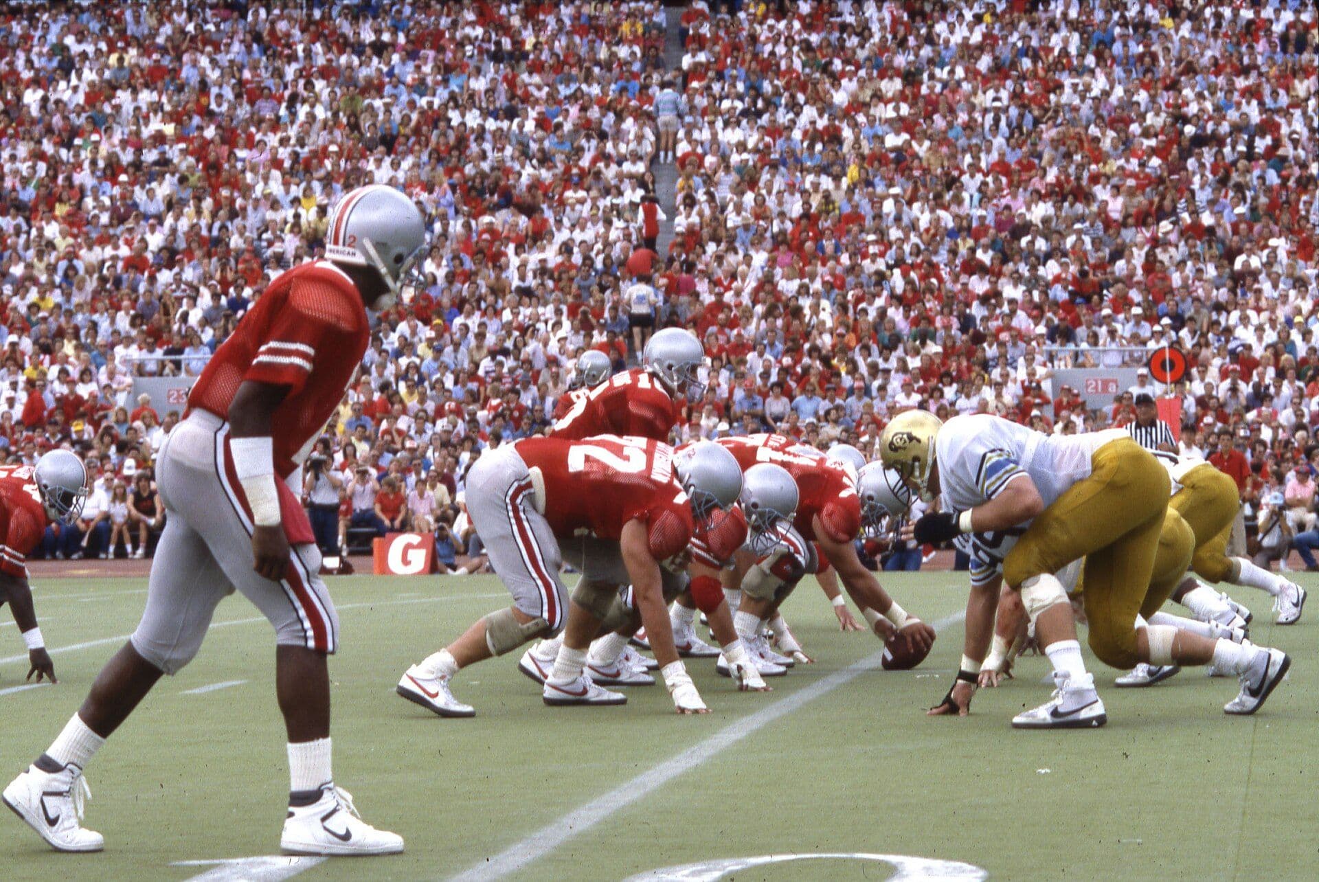 Field-level view of a college football line of scrimmage in front of a packed stadium crowd, an archival 1986 photograph from Ohio Stadium.