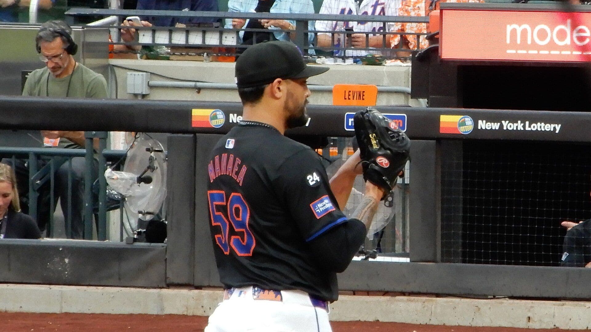 New York Mets pitcher Sean Manaea in a black Mets jersey, number 59, holding his glove in front of the dugout.