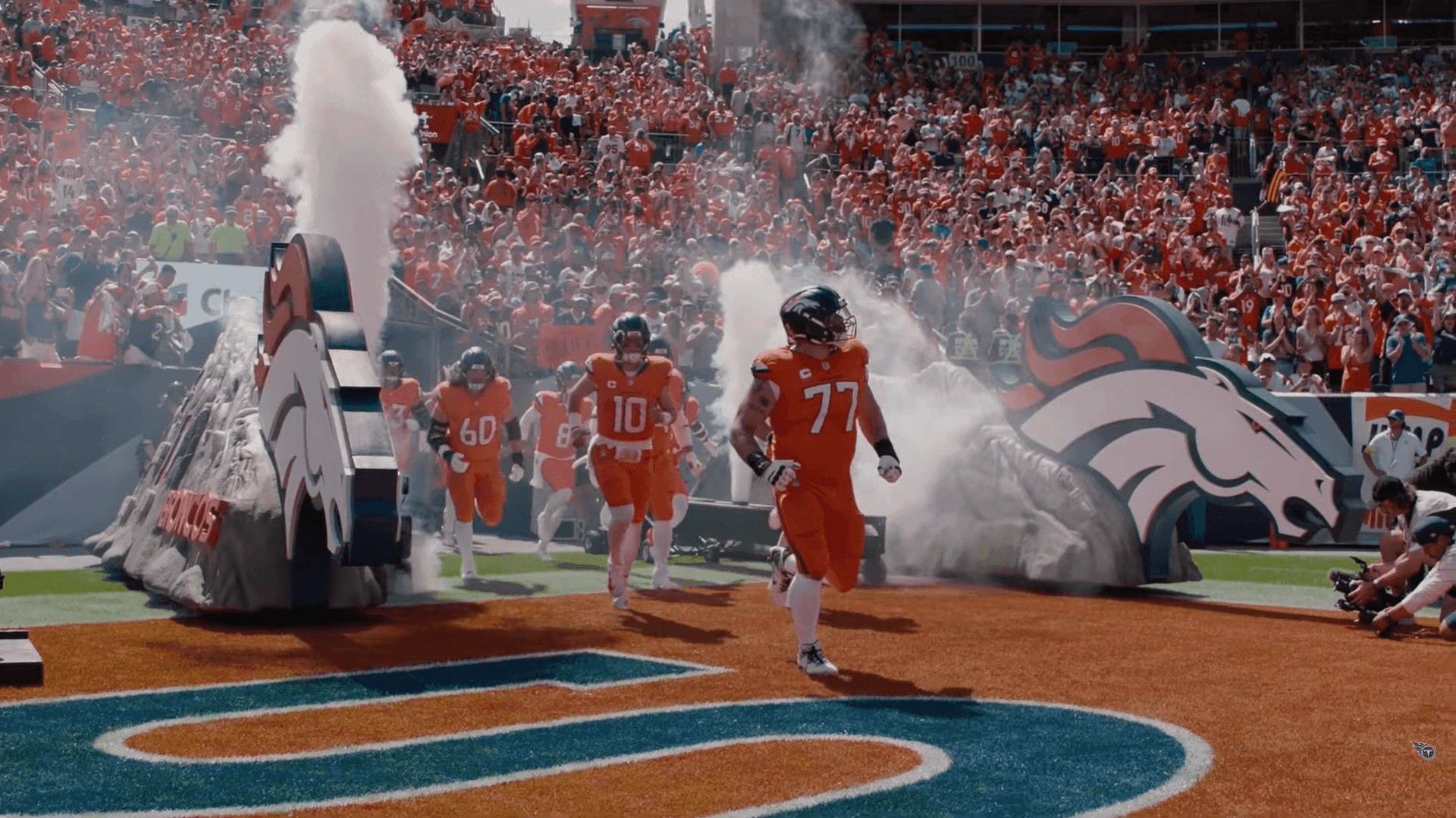 Denver Broncos quarterback Bo Nix, number 10 in the orange home uniform, runs onto the field behind offensive lineman Quinn Meinerz during pregame introductions in front of a packed crowd.